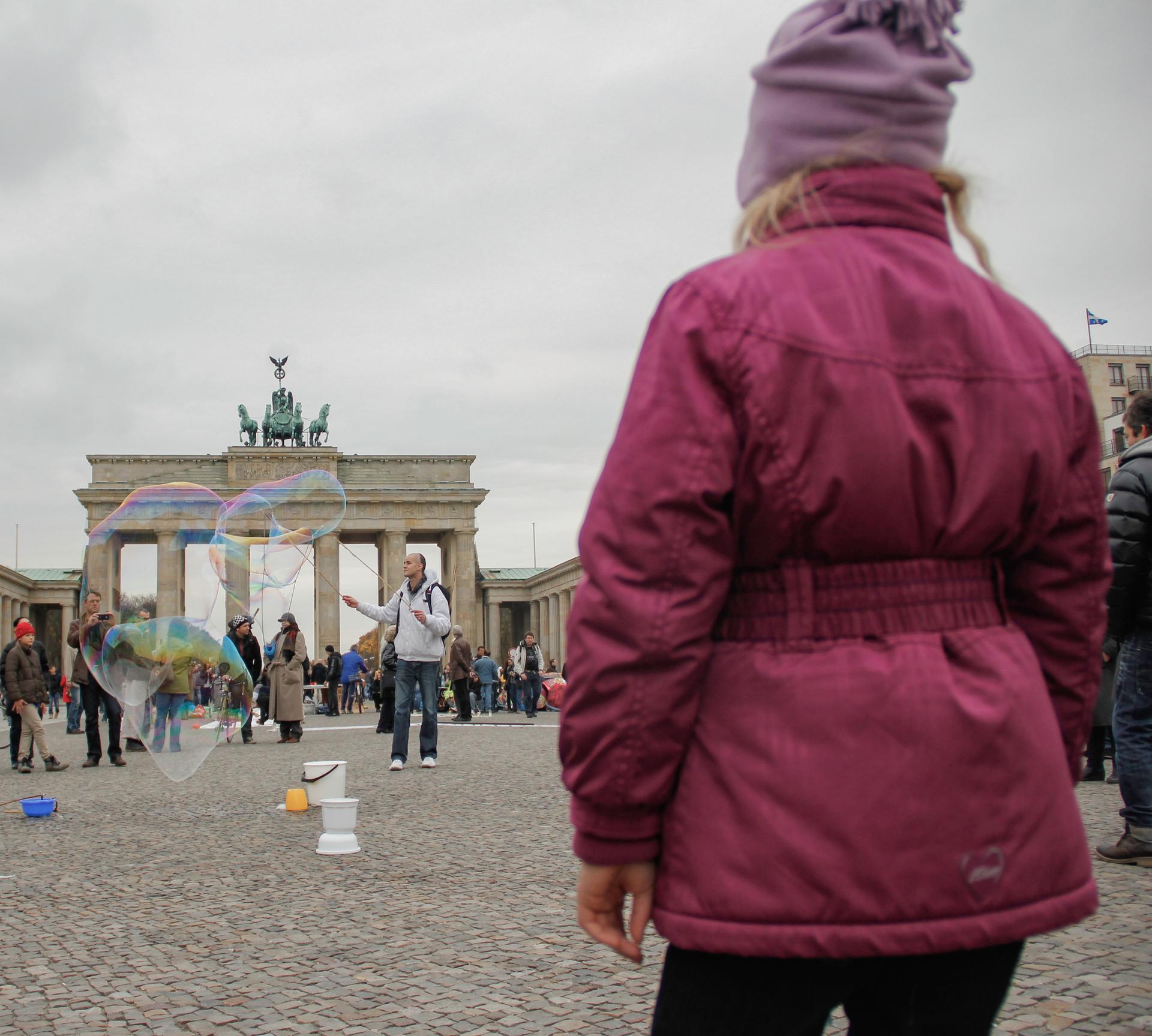 Un enfant de dos regardant des bulles de savons géantes devant la porte de Brandebourg à Berlin