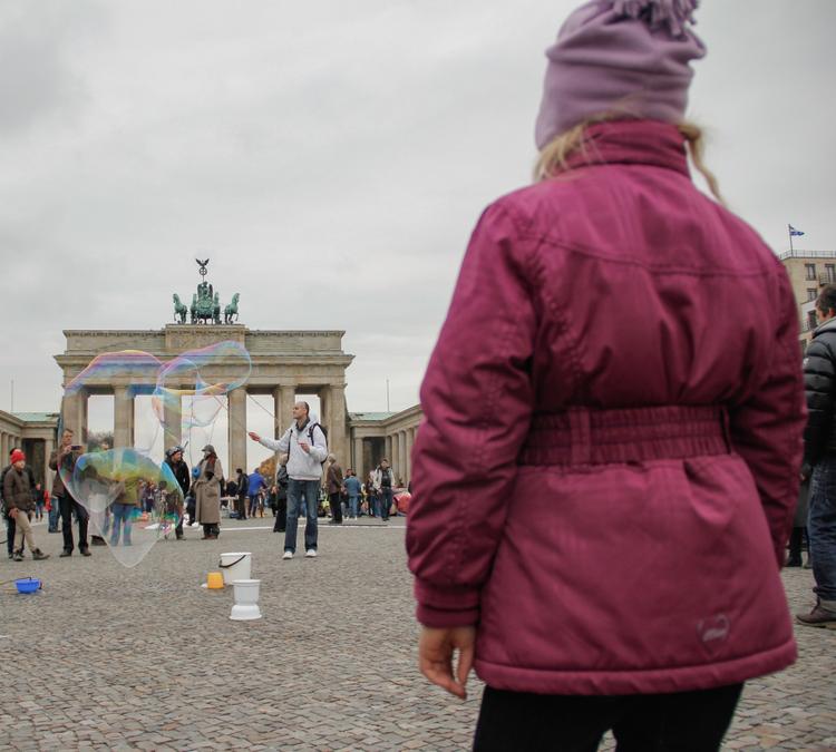 Un enfant de dos regardant des bulles de savons géantes devant la porte de Brandebourg à Berlin