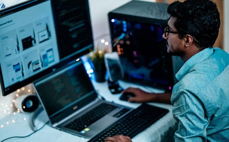 un homme travaille son ordinateur portable, un grand écran et un clavier