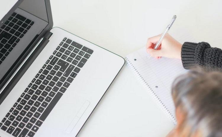 étudiante écrit sur une feuille blanche à côté un ordinateur portable 