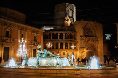 une fontaine sur une place éclairée la nuit