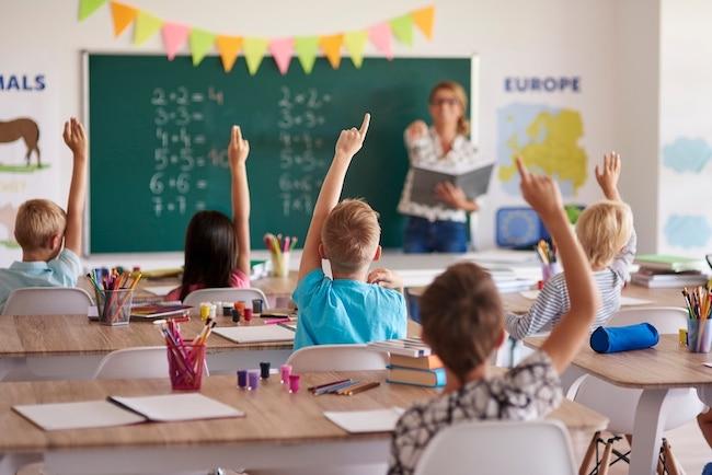 Des eleves lèvent le doigt en classe