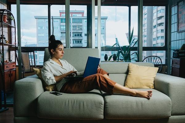 une femme teletravaille sur son sofa