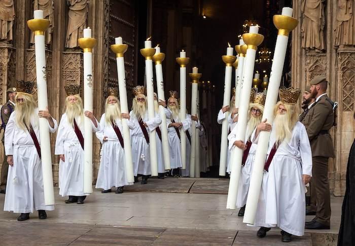 des hommes en blanc avec des cierges immenses lors de la procession du corpus christi à valencia