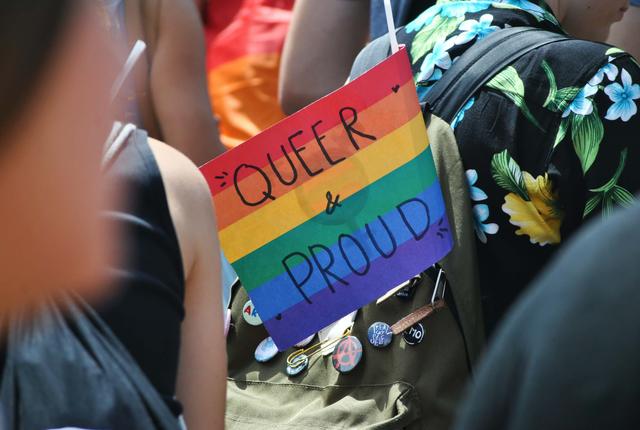 Photo d'un drapeau LGBTQ+ affichant "Queer and proud"