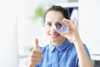 Une femme regardant dans un tube de papier et avec le pouce levé.