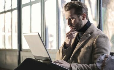 un homme se tient le menton en regardant son ordinateur portable